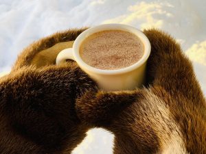 Cup of coffee in fur-mitten-covered hands