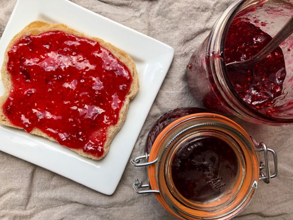 Toast spread with red jam and a jam jar