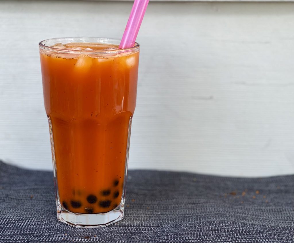 Glass of orange liquid with black balls at the bottom and a pink straw