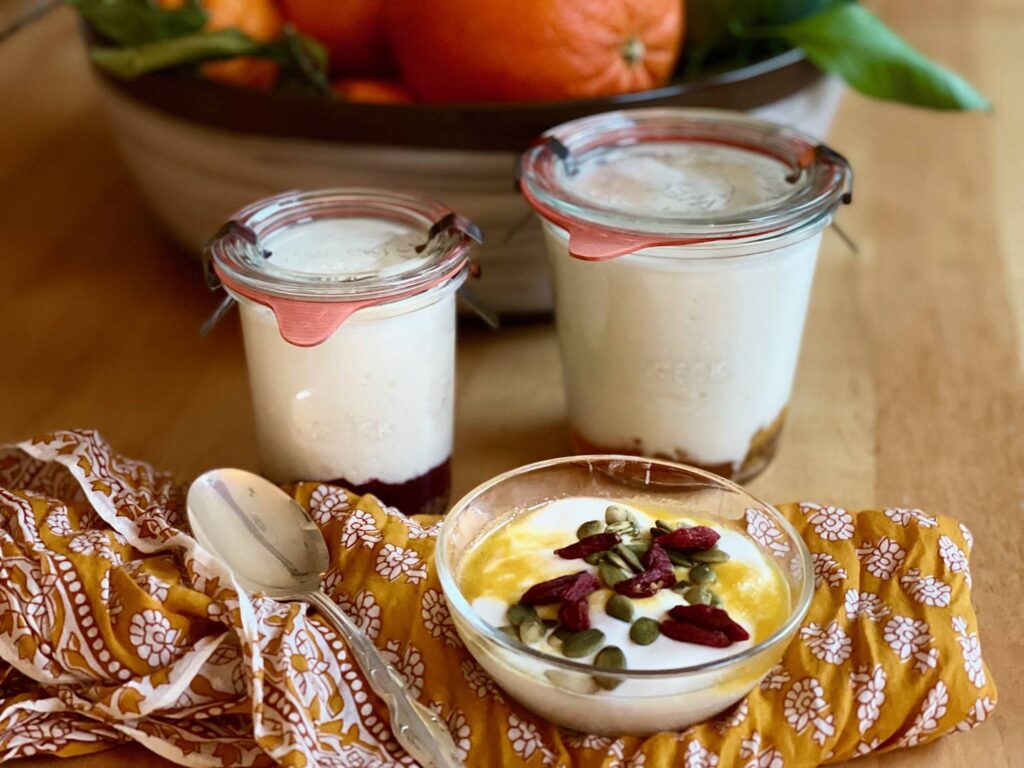 Two jars of yogurt and a bowl of yogurt with a spoon