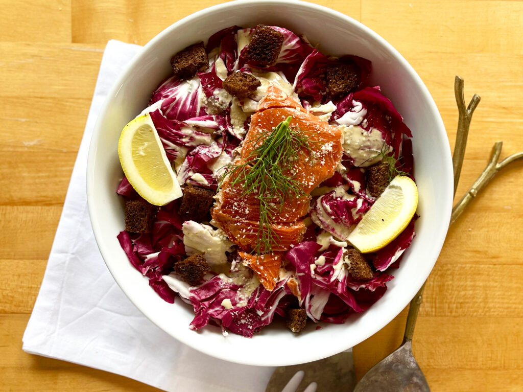 Purple leaves, a piece of smoked salmon and lemons in a white bowl
