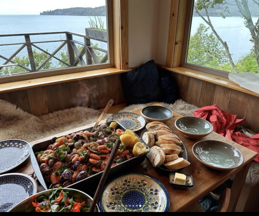 Table with a big pan full of boiled shrimp, corn and potatoes with the ocean in the distance out the windows