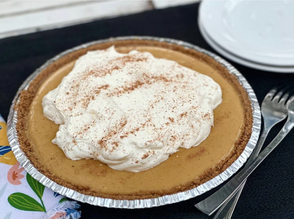 A butterscotch-colored pie in a storebought crust with a big pile of whipped cream on top