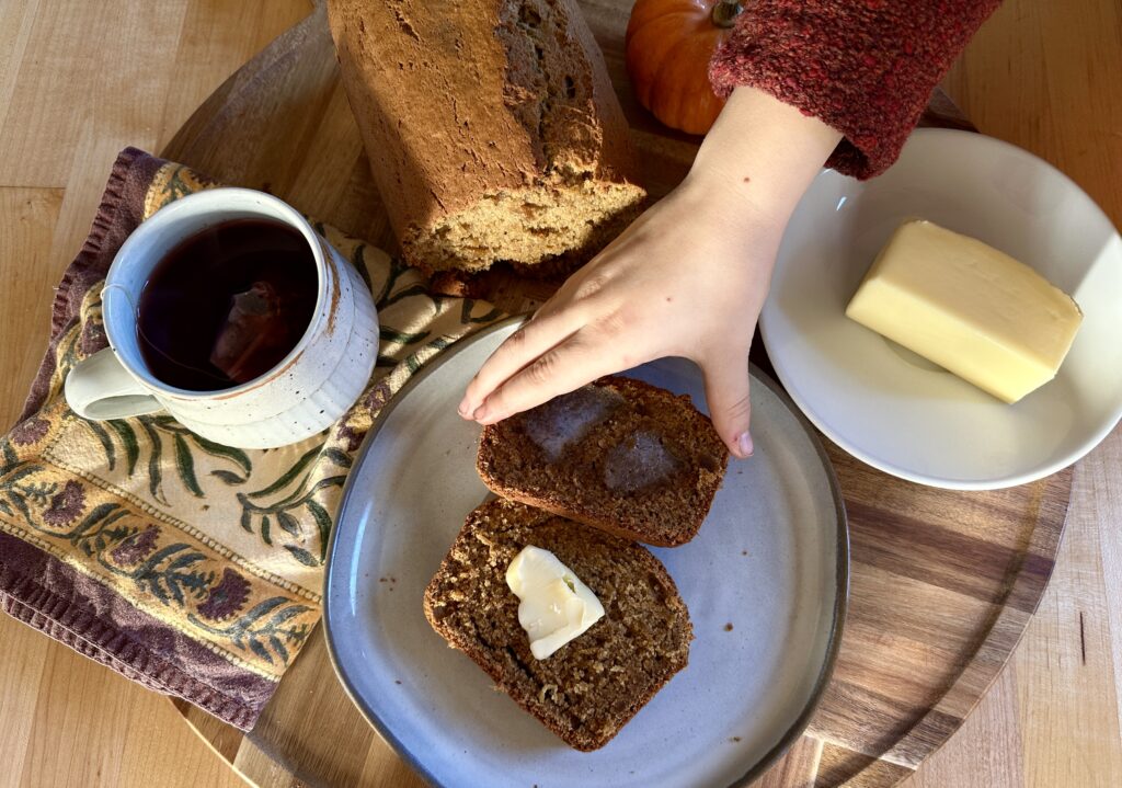 Little girl's hand reaches for a piece of buttered pumpkin bread