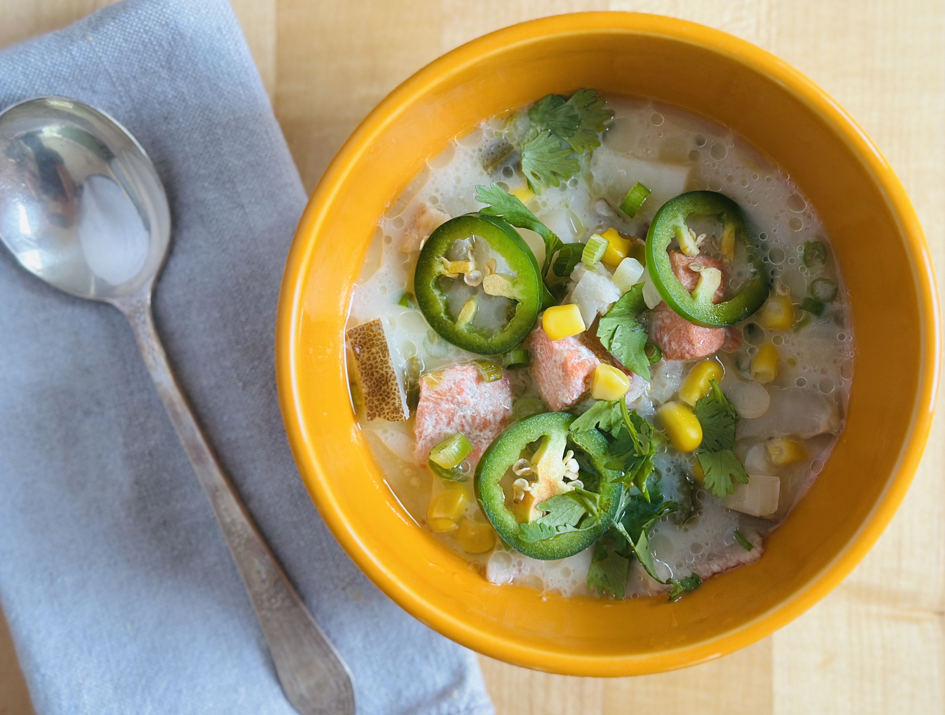 yellow bowl of soup, showing chunks of salmon, potato, jalapeno slices and corn.